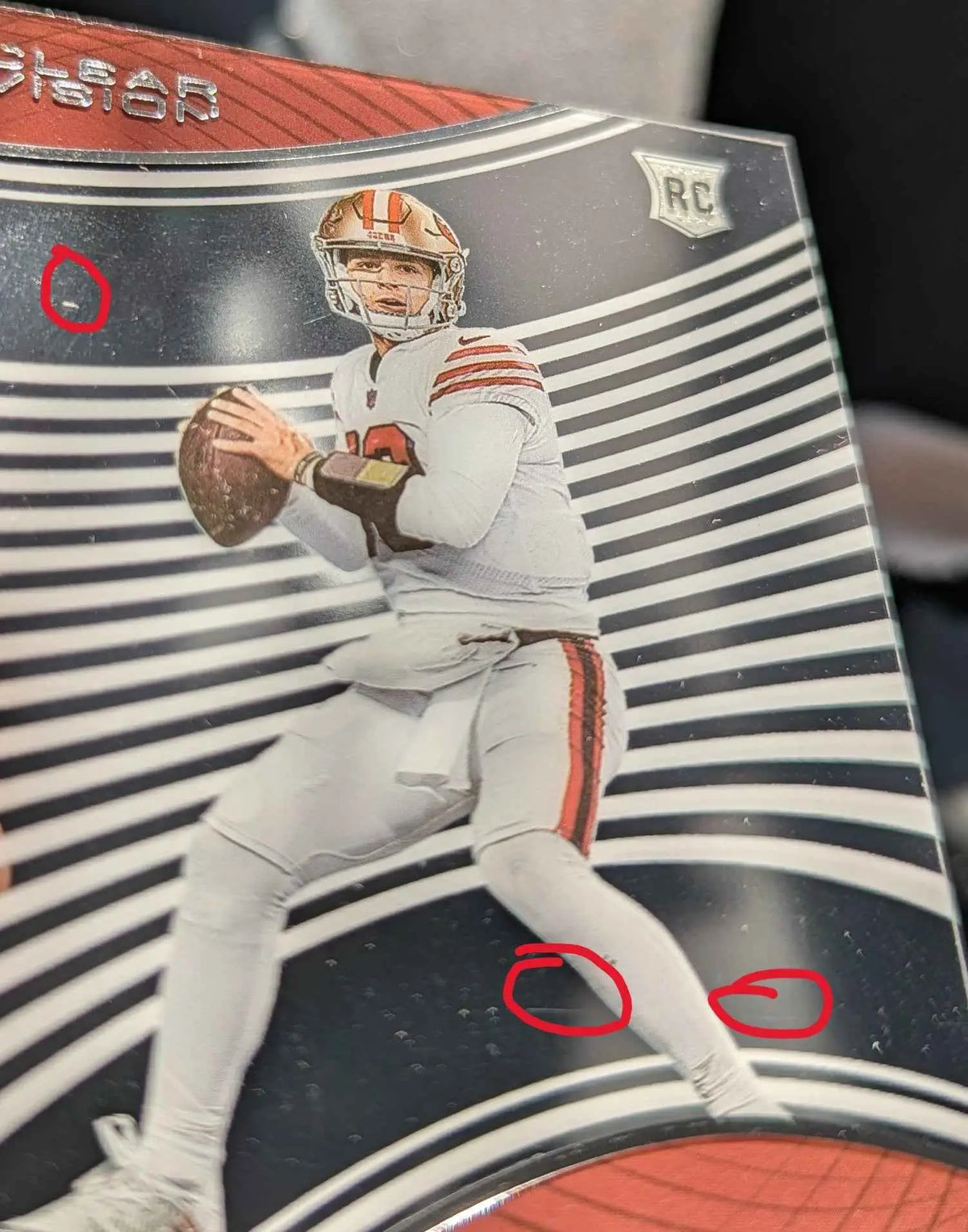 Ein san francisco 49ers rookie card brock purdy 2022 panini chronicles clear vision rookies in weißem uniform mit orange und rot vor schwarz-weiß gestreiftem hintergrund