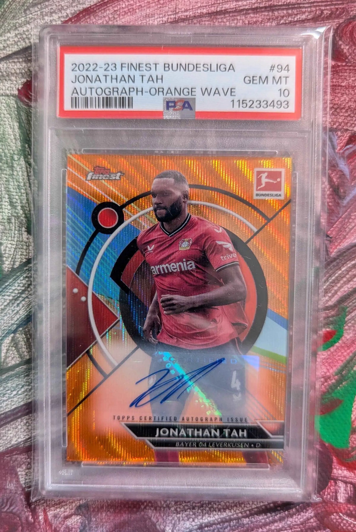 Orange und blaue holografische football trading card mit jonathan tah im roten bayer 04 leverkusen trikot in klarer toplps zertifizierter schutzhülle